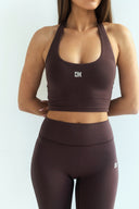 Person wearing a brown sports bra and leggings set with a logo on a light gray background